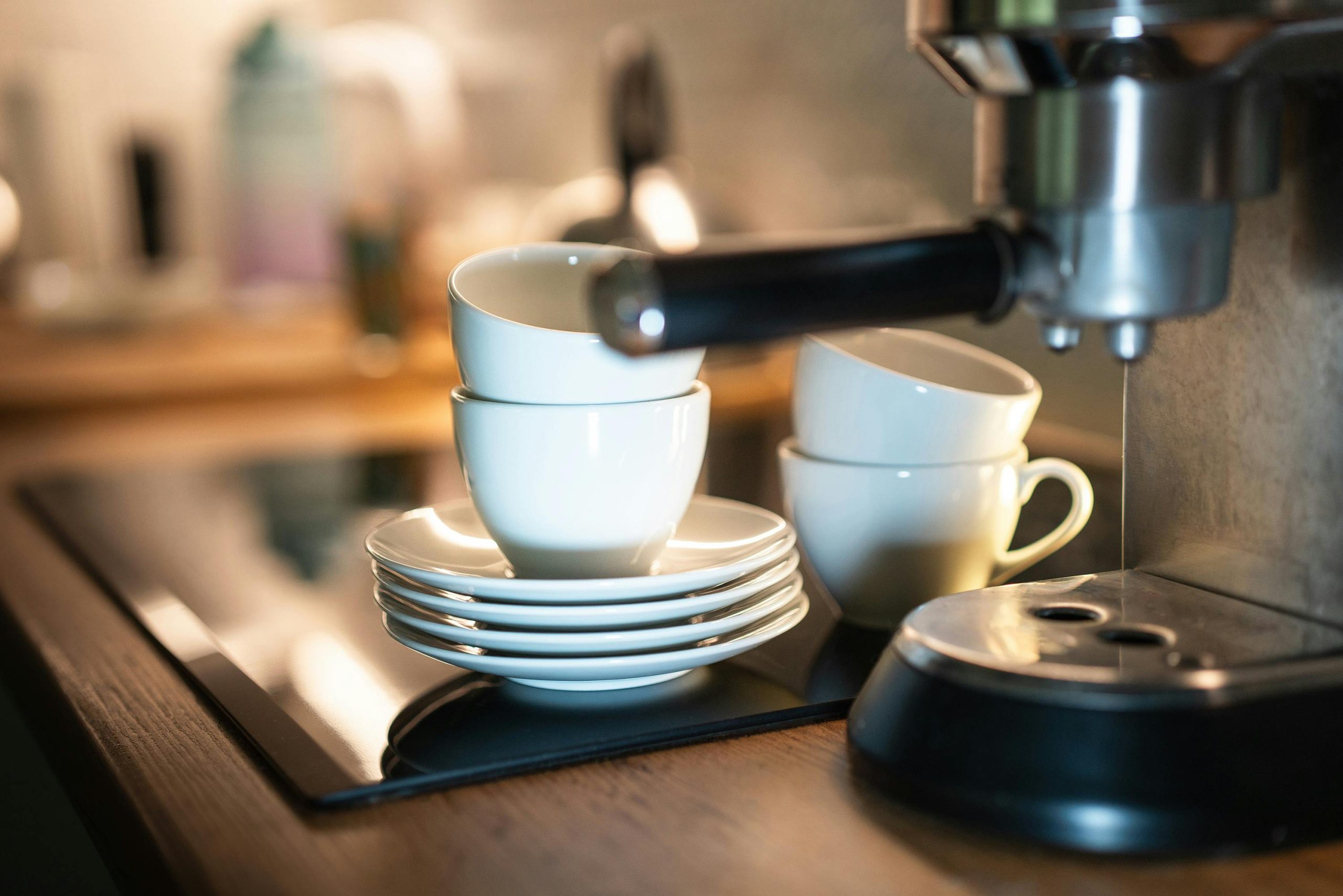 A close-up of an espresso machine with stacked cups in a warm kitchen setting.